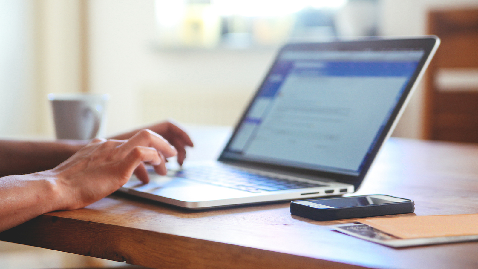 Person at table using a laptop with a smart phone, papers and coffee cup nearby. Person at table using a laptop with a smart phone, papers and coffee cup nearby.