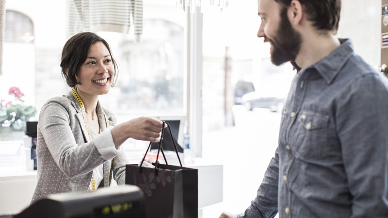 Female design professional giving a shopping bag to customer at cash counter in a studio space.