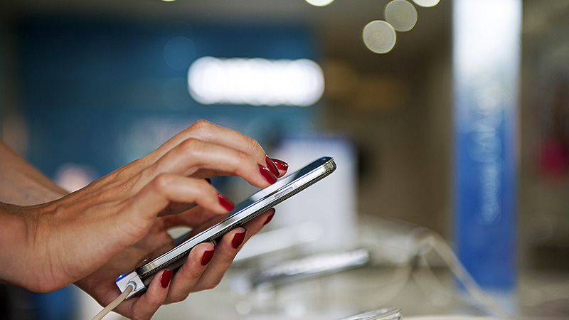 A closeup of a hand holding and interacting with a smart phone.