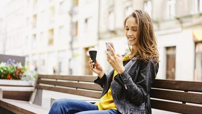 Mujer sentada en un banco mira su celular y come helado